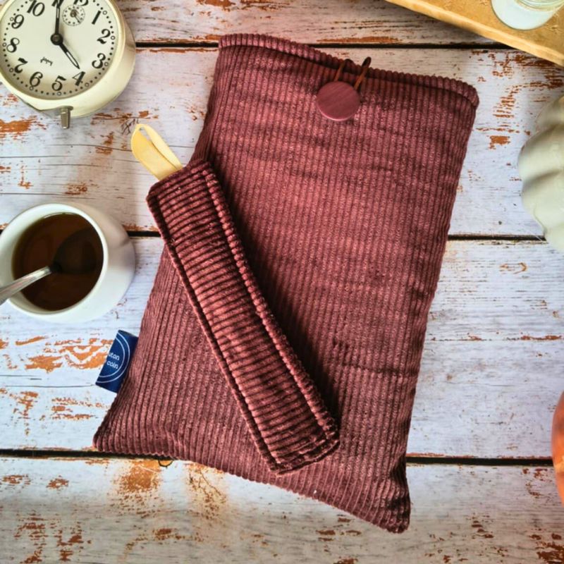 Pochette de livre en velours côtelé marron avec poche avant et bouton assorti, posée sur une table en bois avec tasse de café et ambiance automnale.