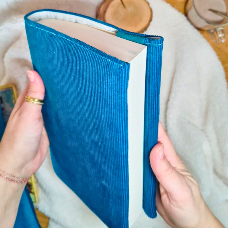 Couverture de livre en velours côtelé bleu roi tenue dans les mains, protégeant un livre et cachant son titre pour une lecture discrète
