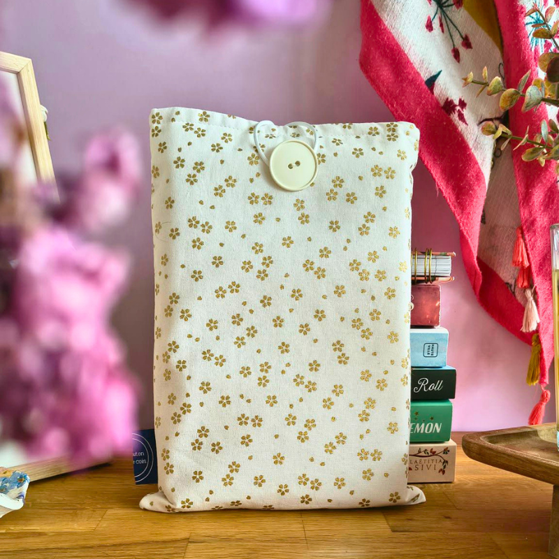 Pochette livre en tissu beige avec petits motifs dorés, idéale pour protéger roman et accessoires de lecture, posée sur table en bois.