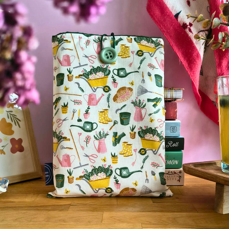 Pochette en tissu avec motifs jardin colorés posée sur une table en bois, décoration intérieure chaleureuse avec fleurs et accessoires autour.